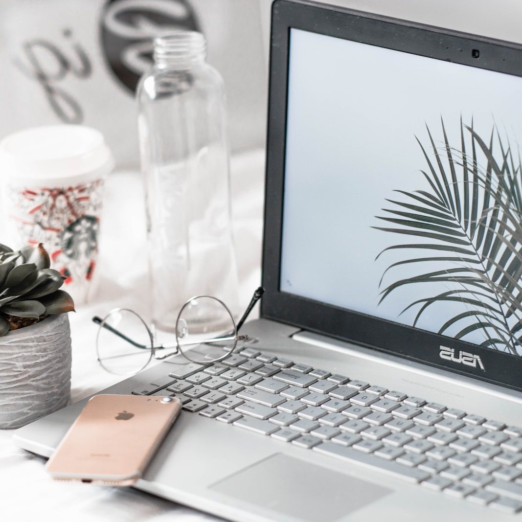 turned-on Asus laptop near eyeglasses, succulent plant, and empty clear glass bottle